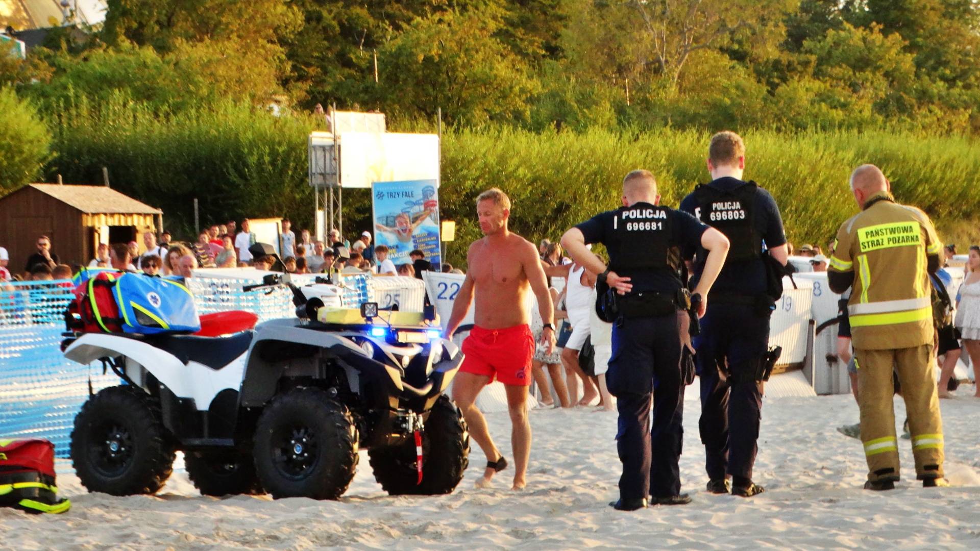 Policjanci, strażak i ratownik przy quadzie medycznym na plaży w Ustce podczas akcji ratunkowej po omdleniu kobiety w morzu
