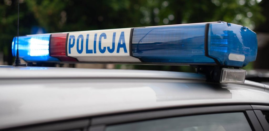 Zbliżenie na belkę sygnalizacyjną na dachu radiowozu policyjnego z widocznym napisem 