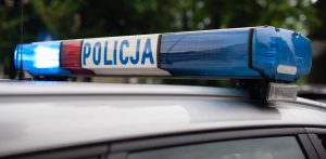 Zbliżenie na belkę sygnalizacyjną na dachu radiowozu policyjnego z widocznym napisem "policja" oraz włączonymi niebieskimi i czerwonymi światłami. Policja apeluje o trzeźwość do kierowców na drodze wojewódzkiej 502 na Mierzeję Wiślaną