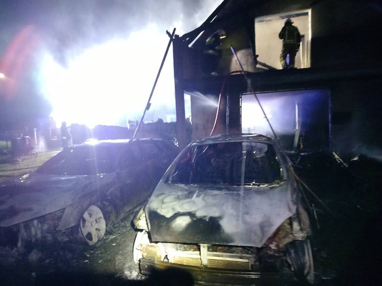 Nocna akcja gaśnicza w Nowęcinie: na pierwszym planie widoczne dwa spalone samochody osobowe oraz zniszczony budynek, w którego oknie stoją strażacy