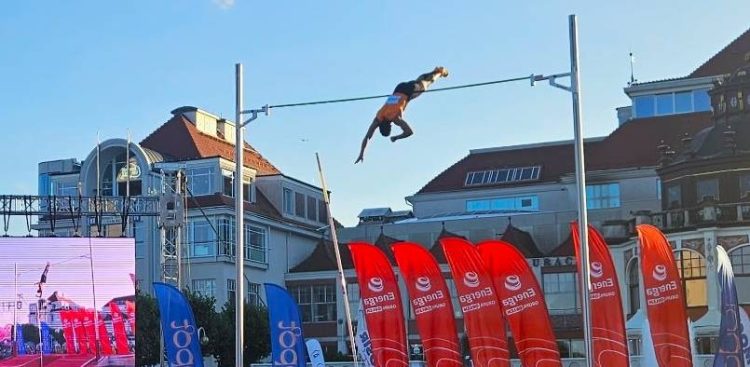 Skok o tyczce podczas mityngu "Tyczka na molo" 2026 w Sopocie - zawodnik w locie pokonuje poprzeczkę na tle sopochich budynków i czerwonych flag sponsorów
