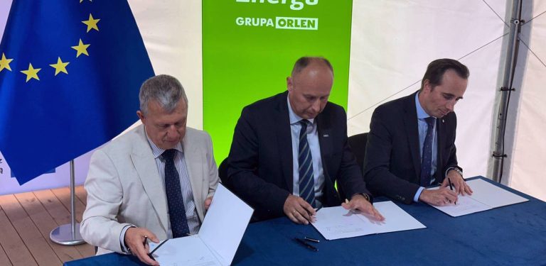 Trzej mężczyźni w garniturach siedzą przy stole i podpisują dokumenty na tle flagi Unii Europejskiej oraz zielonego baneru z logo Energa Grupa ORLEN. W Lubaniu, w powiecie kościerskim, powstanie nowoczesna instalacja agrofotowoltaiczna