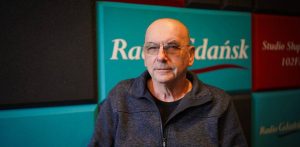Mężczyzna w okularach i ciemnoniebieskiej rozpinanej bluzie na tle zielono-czerwonych paneli akustycznych z logo Radia Gdańsk w Studio Słupsk. To Witold Polkowski, specjalista prawa pracy, który opowiadał o tym, że pracownicy szpitala w Miastku jak najszybciej powinni złożyć wnioski o wypłatę zaległych wynagrodzeń do Funduszu Gwarantowanych Świadczeń Pracowniczych