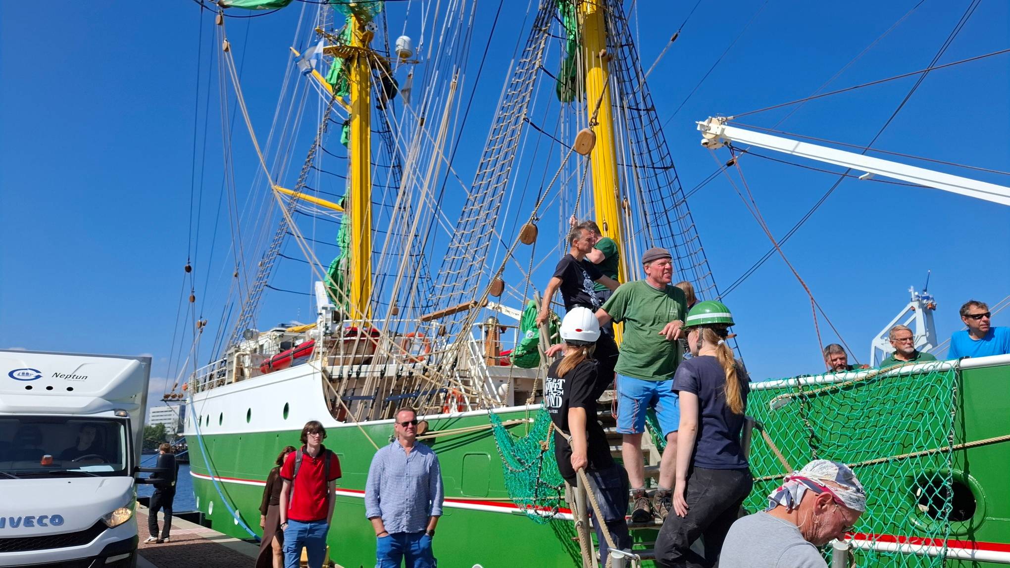 Grupa ludzi wchodzi trapem na pokład zielonego żaglowca szkoleniowego Alexander von Humboldt II. W tle widoczne są żółte maszty, skomplikowane olinowanie i biało-zielony kadłub jednostki zacumowanej w porcie