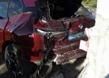 Mocno rozbity tył bordowego samochodu marki BMW po uderzeniu w białą ścianę budynku. Widoczne są silne wgniecenia karoserii, stłuczona tylna szyba oraz uszkodzony zderzak