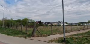 Puste, zielone pole ogrodzone drewnianym płotem w Gdyni Małym Kacku, u zbiegu ulic Strzelców i Żniwnej. W tle widoczne są niskie budynki mieszkalne i zachmurzone niebo. Rada Miasta Gdyni podjęła decyzję o utrzymaniu na tym terenie funkcji rekreacyjno-sportowej