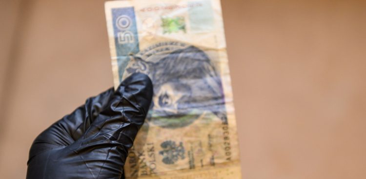 Na zdjęciu osoba w czarnej rękawiczce trzyma banknot 50 zł