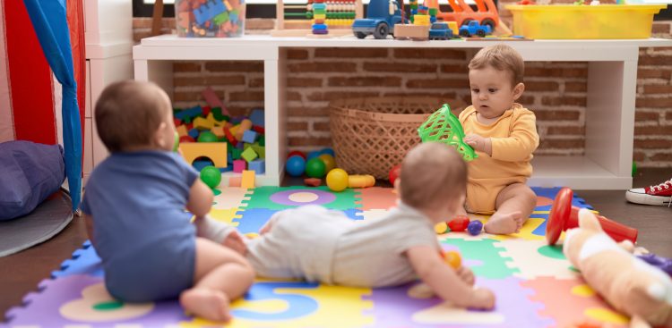 Trójka małych dzieci bawiących się zabawkami na kolorowej macie piankowej w sali żłobkowej. Zdjęcie jest ilustracją do informacji o powstaniu samorządowego żłobka w Rumi