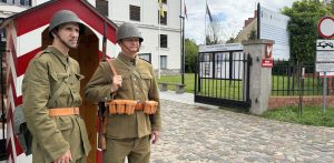 Żołnierze w międzywojennych mundurach stoją przy bramie Muzeum Pomorza Środkowego w Słupsku. Jeden z nich znajduje się tuż obok biało-czerwonej budki wartowniczej, a drugi trzyma karabin