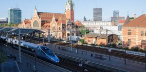 Pociąg Pendolino stojący przy peronie na tle zabytkowego budynku dworca Gdańsk Główny z charakterystyczną wieżą zegarową. do 2034 roku z Trójmiasta wyruszą bezpośrednie pociągi sypialne do Amsterdamu, Kolonii, Tallina czy Wiednia