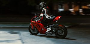 Motocyklista w kasku i skórzanym kombinezonie jedzie nocą na czerwonym motocyklu sportowym po oświetlonej ulicy. Zdjęcie jest ilustracją do artykułu o motocyklach hałasujących nocą w Gdyni