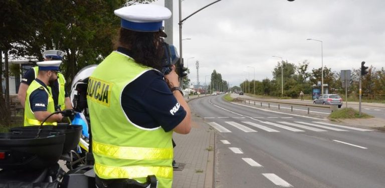 Trzech policjantów w kamizelkach stoi przy drodze, widok z tyłu