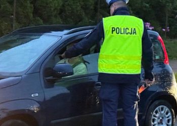 Policjant drogówki w odblaskowej kamizelce przeprowadza kontrolę trzeźwości kierowcy ciemnego samochodu osobowego