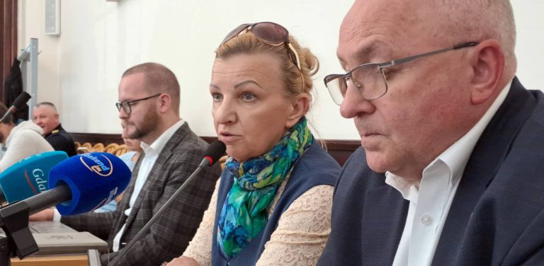Posiedzenie komisji oświaty i zdrowia w Miastku. Kobieta w zielono-niebieskiej chuście (Agnieszka Chrzanowska - przyszła dyrektor szpitala w Miastku) i mężczyzna w okularach siedzą przy stole z mikrofonami podczas posiedzenia komisji, w tle widoczni są inni uczestnicy. Agnieszka Chrzanowska ogłosiła, że komornik zablokował konta szpitala