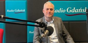 Sebastian Irzykowski z Okręgowej Izby Pielęgniarek i Położnych w rozmowie na temat szpitala w Miastku. Mężczyzna w marynarce siedzi w studiu Studiu Słupsk Radia Gdańsk przed mikrofonem radiowym