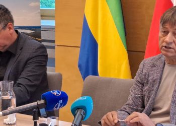 Od lewej: zastępca wójta gminy Chojnice Janusz Szczepański i wójt Zbigniew Szczepański. Mężczyźni siedzą przy stole konferencyjnym z mikrofonami. Wójt przemawia. W tle widoczne są flagi oraz grafika przedstawiająca jezioro. Zdjęcie ilustruje news o tym, że gmina Chojnice zorganizuje szkolenie dla wszystkich sołtysów