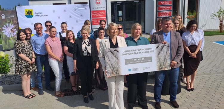 Grupa osób stoi przed Urzędem Gminy Parchowo. Trzymają wspólnie czek z napisem "USUWANIE WYROBÓW ZAWIERAJĄCYCH AZBEST. 1 593 572 ZŁ DLA WOJEWÓDZTWA POMORSKIEGO"