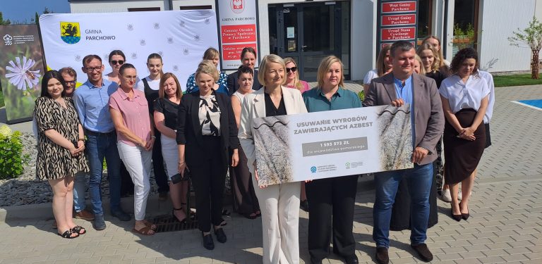 Grupa osób stoi przed Urzędem Gminy Parchowo. Trzymają wspólnie czek z napisem "USUWANIE WYROBÓW ZAWIERAJĄCYCH AZBEST. 1 593 572 ZŁ DLA WOJEWÓDZTWA POMORSKIEGO"