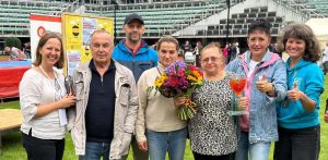 Grupa siedmiu uśmiechniętych osób stoi pozując do zdjęcia na tle trybun stadionu sportowego