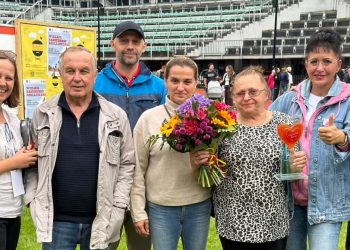 Grupa siedmiu uśmiechniętych osób stoi pozując do zdjęcia na tle trybun stadionu sportowego