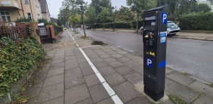 Ciemnoszary, nowoczesny parkomat z niebieskim symbolem "P", stojący na chodniku przy ulicy w strefie płatnego parkowania. W minionym sezonie wakacyjnym Ustka zanotowała z tytułu opłat postojowych rekordowe 2,5 mln zł dochodu - ponad dwukrotnie więcej niż w roku ubiegłym