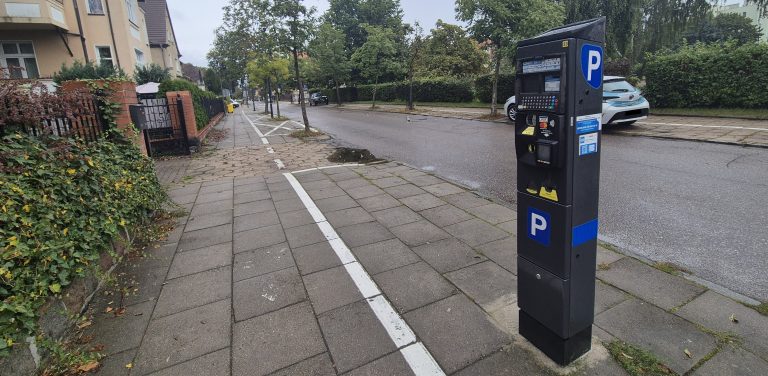 Ciemnoszary, nowoczesny parkomat z niebieskim symbolem "P", stojący na chodniku przy ulicy w strefie płatnego parkowania. W minionym sezonie wakacyjnym Ustka zanotowała z tytułu opłat postojowych rekordowe 2,5 mln zł dochodu - ponad dwukrotnie więcej niż w roku ubiegłym