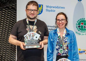 Uśmiechnięte małżeństwo brydżystów, Piotr i Agnieszka Wiankowscy, pozuje na tle ścianki sponsorskiej mistrzostw świata. Mężczyzna trzyma puchar za drugie miejsce z motywem katowickiego Spodka i kart do gry, a kobieta ma na szyi pamiątkowy medal