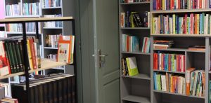 Wnętrze nowoczesnej biblioteki: wysokie, szare regały gęsto zapełnione kolorowymi książkami oraz uchylone drzwi pośrodku