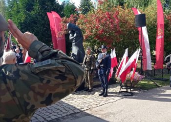 Światowy Dzień Sybiraka w Gdańsku. Żołnierz salutujący przed Pomnikiem Golgoty Wschodu na Cmentarzu Łostowickim w Gdańsku. Przy pomniku stoi warta honorowa w otoczeniu biało-czerwonych flag i flag Gdańska.