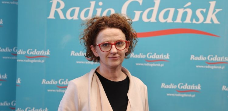 Kobieta w okularach w czerwonych oprawkach i jasnej narzutce na tle niebieskiej ścianki z logo Radia Gdańsk - pełnomocniczka prezydenta Sopotu ds. praw człowieka i koordynatorka Sopockiej Jesieni Zdrowia Psychicznego