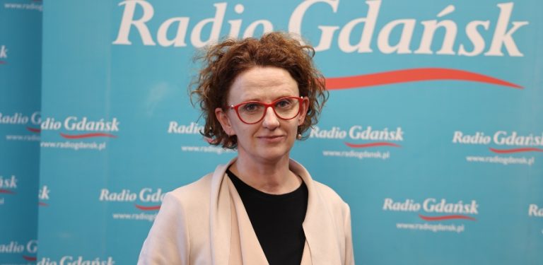 Kobieta w okularach w czerwonych oprawkach i jasnej narzutce na tle niebieskiej ścianki z logo Radia Gdańsk - pełnomocniczka prezydenta Sopotu ds. praw człowieka i koordynatorka Sopockiej Jesieni Zdrowia Psychicznego