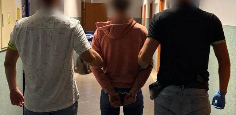 Dwaj nieumundurowani policjanci prowadzą korytarzem skutą kajdankami kobietę w różowej bluzie z kapturem, podejrzaną o podpalenie wiaty śmietnikowej oraz supermarketu na gdańskiej Oruni. Głowy osób na zdjęciu są zamazane
