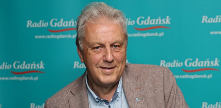 Mężczyzna siwy, uśmiechnięty przed mikrofonem.