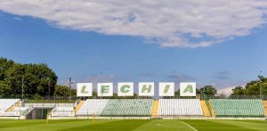 Pusta trybuna z biało-zielonymi krzesełkami i dużym białym napisem "LECHIA" na stadionie przy ul. Traugutta w Gdańsku, w tle zielone drzewa i błękitne niebo. Miasto Gdańsk. W ramach wartej 7 mln zł umowy promocyjnej Lechia Gdańsk będzie korzystać z miejskich obiektów i promować miasto w 1. Lidze, walcząc o powrót do Ekstraklasy