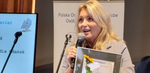 Beata Gwoździewicz przemawia do mikrofonu, trzymając w rękach pamiątkowy certyfikat konkursu "Lodołamacze 2026". W tle widoczny ekran z prezentacją i logo POPON.
