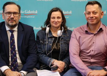 Na kanapie siedzi dwóch mężczyzn i pomiędzy nimi kobieta. Patrzą w kamerę, za nimi ścianka z logiem Radia Gdańsk.