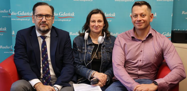 Na kanapie siedzi dwóch mężczyzn i pomiędzy nimi kobieta. Patrzą w kamerę, za nimi ścianka z logiem Radia Gdańsk.