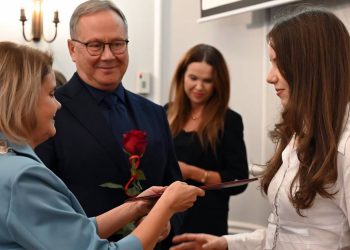 Przewodnicząca Rady Miasta Starogard Gdański Anna Benert w uroczystym łańcuchu oraz prezydent Janusz Stankowiak trzymający czerwoną różę wręczają pamiątkowy dyplom maturzystce Marcie Derron