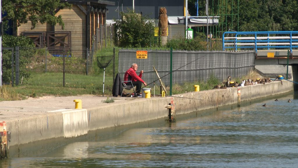 Wędkarz siedzący na nabrzeżu w porcie w Rowach, łowiący ryby w kanale