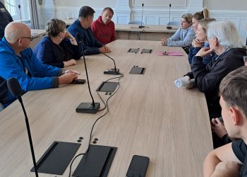 Przy stole na którym stoją mikrofony siedzą młodzi i starsi ludzie.