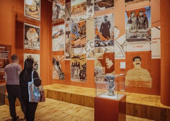 Dwoje zwiedzających ogląda ekspozycję w Muzeum II Wojny Światowej w Gdańsku. Na pomarańczowej ścianie wiszą radzieckie plakaty propagandowe przedstawiające m.in. Józefa Stalina, a na podeście w szklanej gablocie stoi niewielkie popiersie. Placówka, we współpracy z kołem PSONI, przygotowała nowe ścieżki zwiedzania dostosowane do potrzeb osób z niepełnosprawnością intelektualną, w tym materiały w tekście łatwym do zrozumienia (ETR) oraz audioprzewodnik czytany przez Annę Dymną