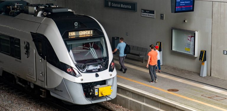 Pociąg Newag Impuls stojący przy peronie przystanku Gdańsk Matarnia, obok pasażerowie na peronie.Na trasie Pomorskiej Kolei Metropolitalnej w godzinach szczytu kursują podwójne składy, które mają rozładować poranny i popołudniowy tłok