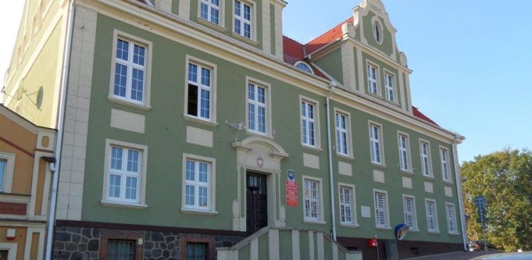 Zabytkowy, piętrowy budynek Urzędu Miejskiego w Skarszewach o zielonej elewacji ze sztukateriami, kamienną podmurówką, ozdobnym szczytem oraz wejściem po schodach, przy którym wiszą czerwone tablice urzędowe z godłem Polski