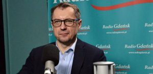 Sławomir Kiszkurno w okularach i ciemnej marynarce przed mikrofonem w studiu Radia Gdańsk. W audycji "Gość Radia Gdańsk" mówił o stratach finansowych i wyzwaniach dla gospodarki odpadami po wprowadzeniu systemu kaucyjnego
