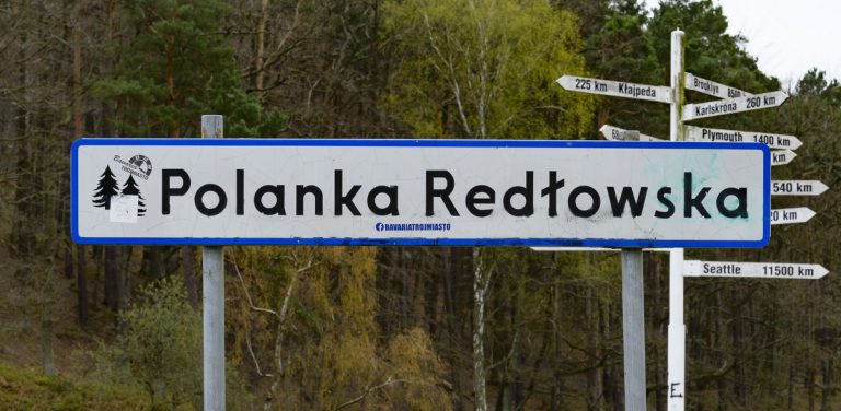 Na zdjęciu znajduje się napis Polanka Redłowska. Zdjęcie na tle lasu.