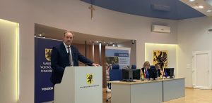 Marszałek województwa pomorskiego Mieczysław Struk przemawia przy mównicy z herbem województwa podczas konferencji prasowej w Urzędzie Marszałkowskim w Gdańsku. W tle widoczny jest stół prezydialny oraz banery promocyjne Funduszy Europejskich dla Pomorza