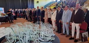 Uczestnicy uroczystości jubileuszowej stojący w hali, z grawerowanymi szklanymi statuetkami na pierwszym planie