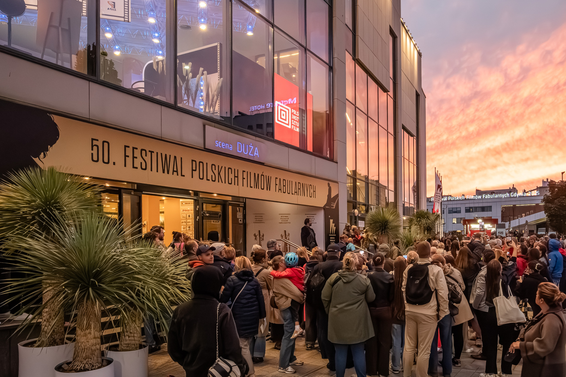Tłum publiczności zgromadzony przed wejściem na Scenę Dużą Teatru Muzycznego w Gdyni pod banerem 50. FPFF na tle pomarańczowego nieba o zachodzie słońca