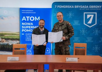 Przedstawiciel spółki Polskie Elektrownie Jądrowe i dowódca 7. Pomorskiej Brygady Obrony Terytorialnej stoją za stołem i prezentują podpisany dokument. W tle widać baner informacyjny o energii jądrowej na Pomorzu oraz ściankę 7PBOT z flagą Polski