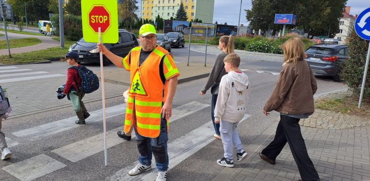 Na zdjęciu przeprowadzacz w jaskrawym oznaczeniu przeprowadza osoby przez przejście